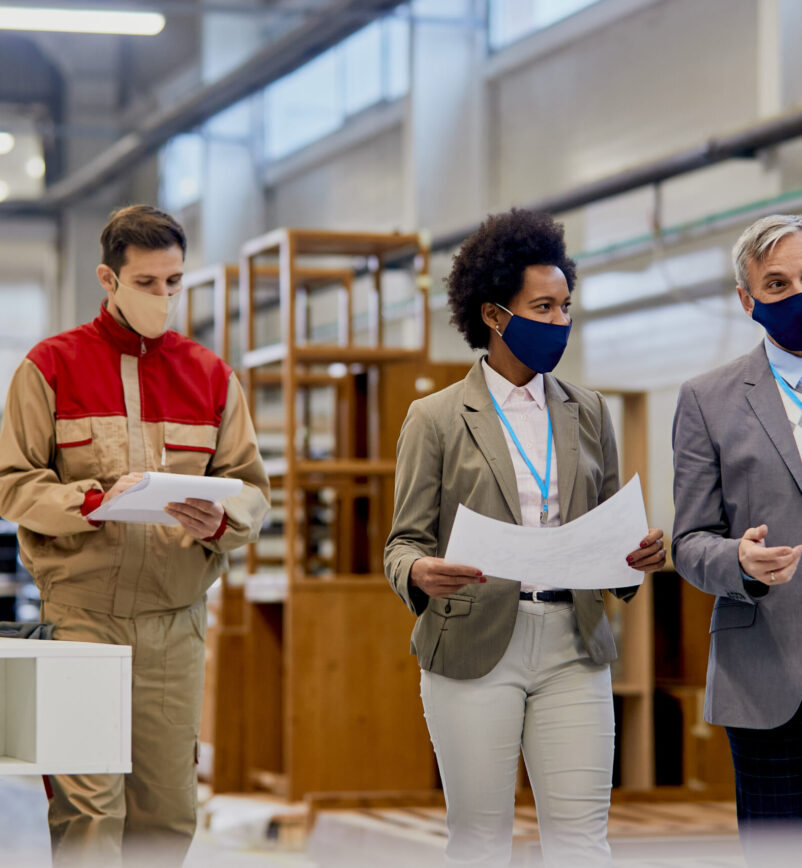 Company managers with protective face masks talking while visiting wood factory facility.